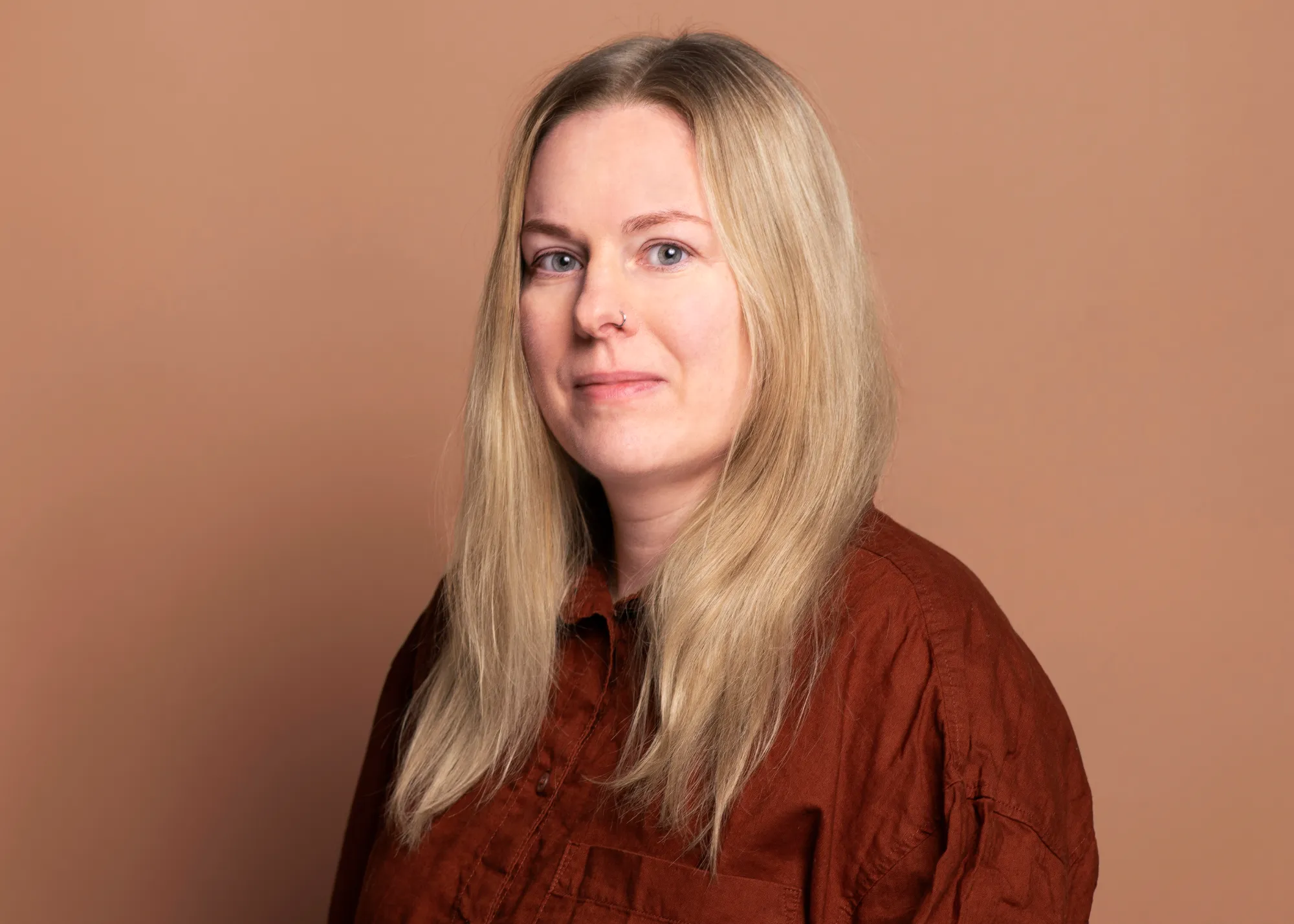 Porträt von Katrin Sellerbeck. Sie schaut freundlich in die Kamera. Sie trägt ein dunkelrotes Hemd und ihre hellblonden Haare offen.