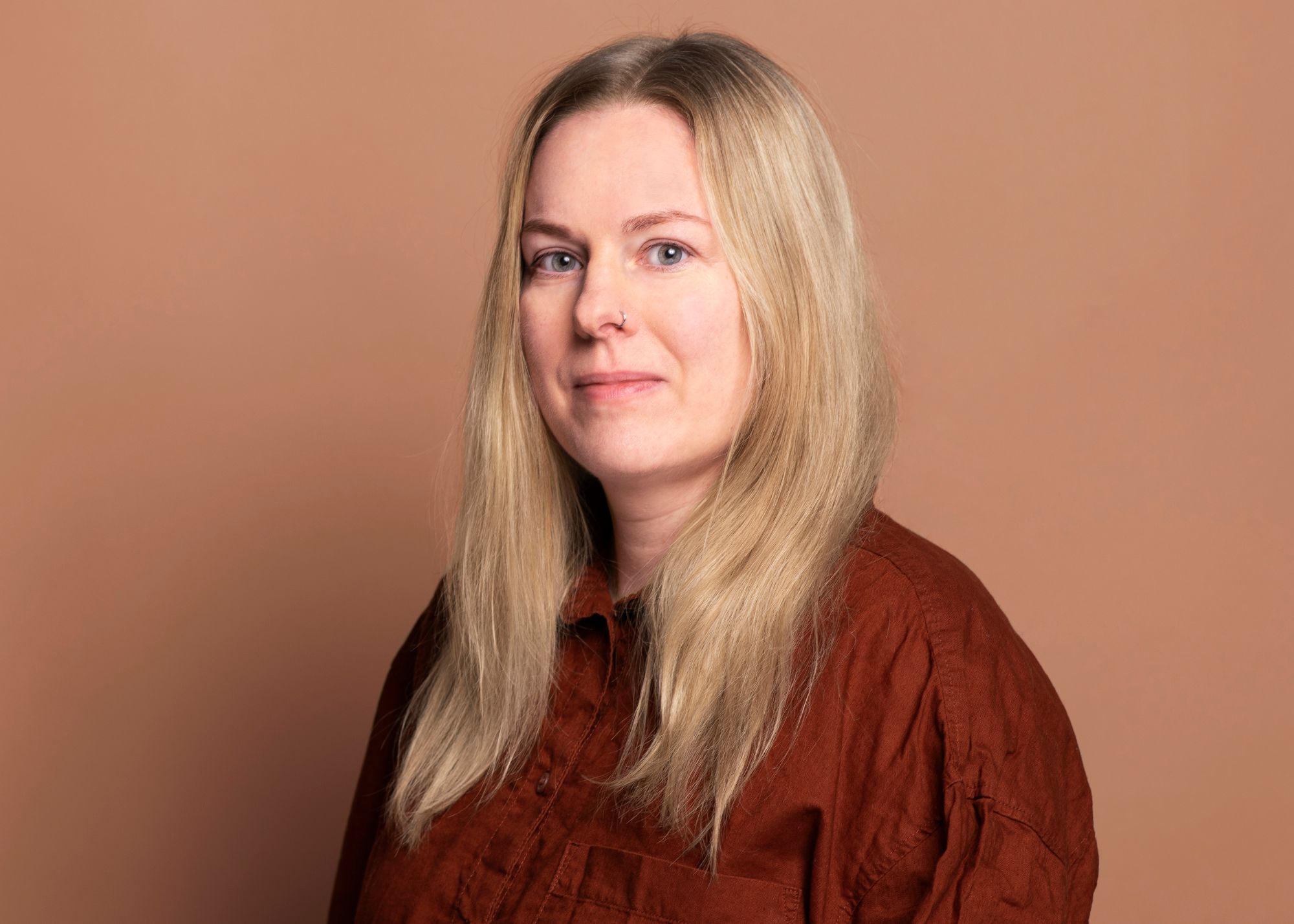 Porträt von Katrin Sellerbeck. Sie schaut freundlich in die Kamera. Sie trägt ein dunkelrotes Hemd und ihre hellblonden Haare offen.